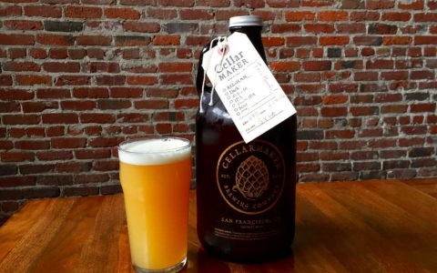 Cellarmaker Brewery Growler next to a glass of beer in front of an exposed brick wall